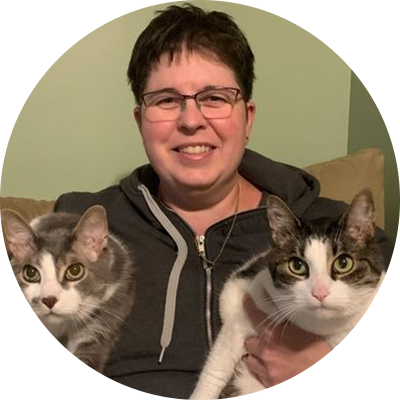 A woman holding two cats in her arms.